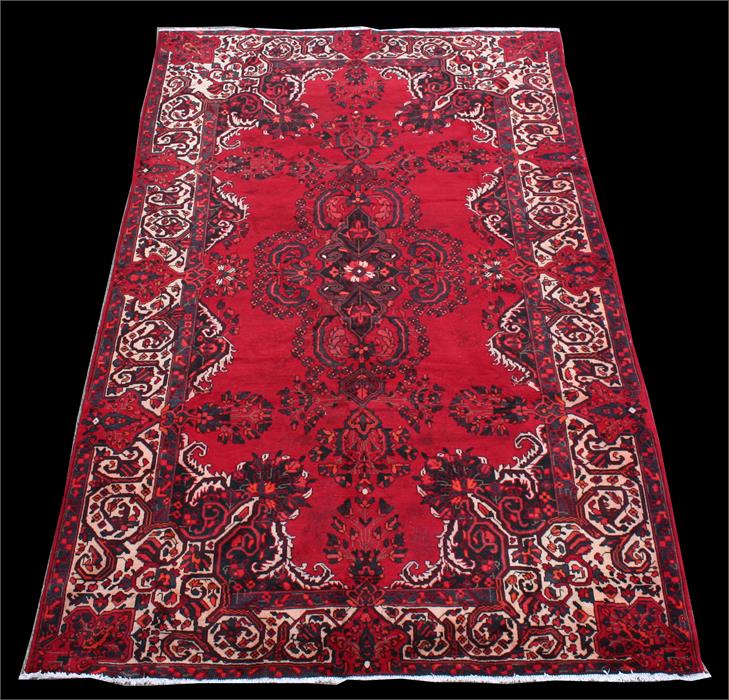 A Persian Feridan woollen hand made rug with stylised flowers and geometric borders, on red