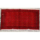 A Turkoman woollen hand-made rug with geometric designs on a red ground, 110 by 55cms (43 by 21.