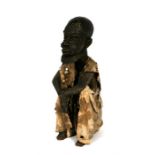An African wooden figure in the form of a seated bearded man wearing a robe decorated with sea