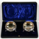 A cased pair of Victorian silver salts with embossed foliate decoration, standing on three short