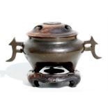 A bronze censer inlaid with silver wire decoration and shaped lugged handles, with carved wooden