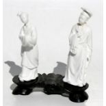 A pair of Chinese blanc de chine figures mounted on a carved hardwood stand, the largest figure