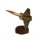 A brass apprentice piece jet fighter on a stand, with a wingspan of 13 by 15.5cms (5 by 6ins) long.