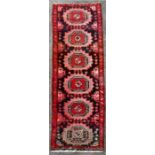 A Persian Ardabil woollen runner with repeated geometric medallions on a red ground, 296 by 80cms (