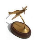A brass model of a WW2 climbing Spitfire standing on a wooden base. Wingspan 10cms (4ins) by 9.