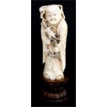 A 19th century Chinese ivory figure depicting Lohan holding a dragon, mounted on a hardwood stand,