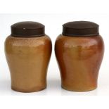 Two brown stoneware jars, possibly Leach jars, with painted tin covers, 22cms (8.5ins) high.