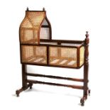 A Victorian mahogany swinging bassinet with bergere caned sides and Gothic form hood, on turned