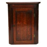 A Georgian oak corner cupboard, the panelled door enclosing a shelved interior, 74cms (29ins) wide.