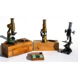 Two lacquered brass student microscopes, boxed; another microscope, together with a box of