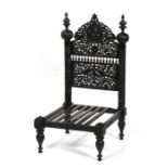 An Indian hardwood low chair profusely pierced and carved with birds, flowers and figures.