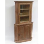 A late Victorian pine two section corner cupboard, the top with glazed door enclosing shelves the