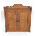 A small late Victorian pitch pine wall mounted cabinet, the pair of panelled doors enclosing shelved