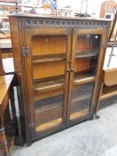 Oak glazed cabinet with carved decoration, the two glazed doors revealing three shelves,