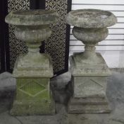 Pair of reconstituted stone garden urns, raised on plinth bases,