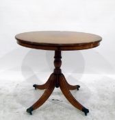 Reproduction yew wood circular table on reeded turned supports with brass claw feet and castors