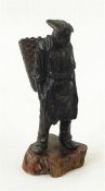 Bronzed figure of a man carrying wicker basket, standing (possibly missing pipe), on a wooden plinth