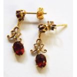 Pair of gold-coloured metal and garnet stone pendant drop earrings, each with garnet studs, scroll