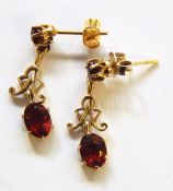 Pair of gold-coloured metal and garnet stone pendant drop earrings, each with garnet studs, scroll
