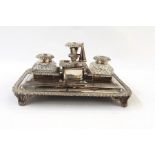 Silver plated inkstand with cut glass inkwells, on four pad feet, with a central candle holder and