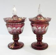 Pair of Victorian cranberry glass pedestal lidded urns with clear glass finials, rose etched
