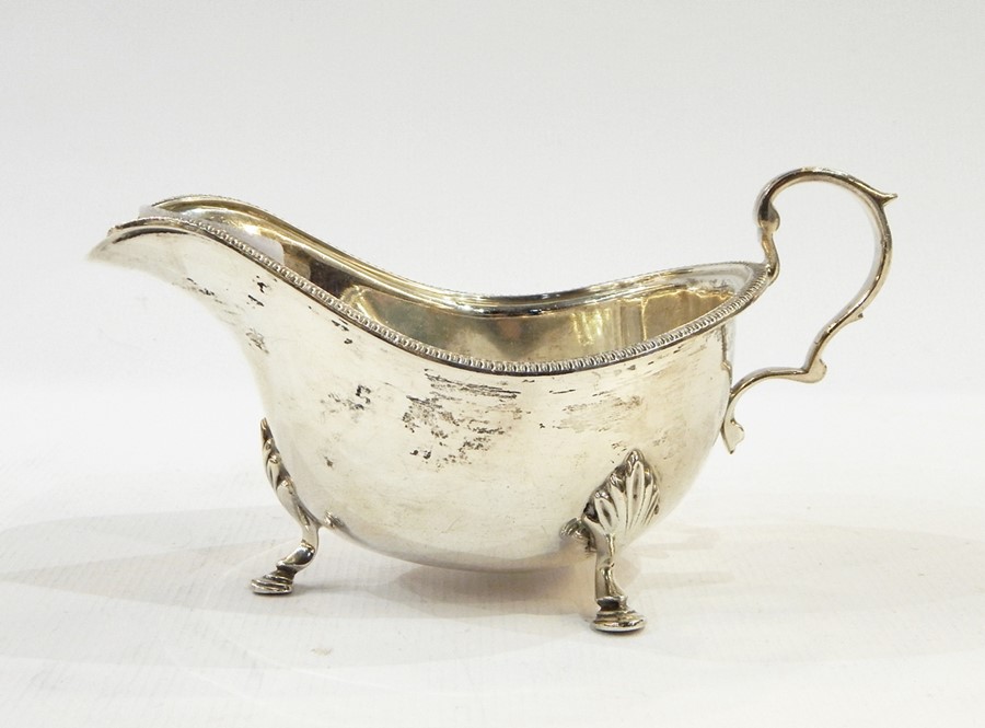 George VI silver sauceboat of Georgian-style with gadrooned rim, scroll handle, raised on three
