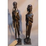 Two Kenyan carved ebonised wooden figures of man and a women in traditional dress, raised on stepped