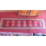 A Kazak runner with repeating geometric motifs on a red field contained by leaf border on a beige