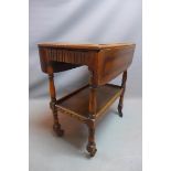 An early 20th century oak two tier drop leaf drinks trolley raised on turned legs and castors. H-