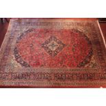 A fine Persian Kashan carpet with central floral medallion on a rouge field with tri colour