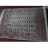 A Bokhara style rug with elephant pad motifs on a beige ground contained by geometrical borders.