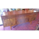 A mid 20th century rosewood sideboard with three drawers over four cupboard doors raised on teak