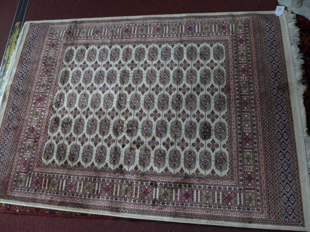 A Bokhara style rug with elephant pad motifs on a beige ground contained by geometrical borders.