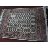 A Bokhara style rug with elephant pad motifs on a beige ground contained by geometrical borders.