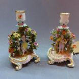 A pair of Meissen candlesticks with central figures surrounded with foliage. H.18cm