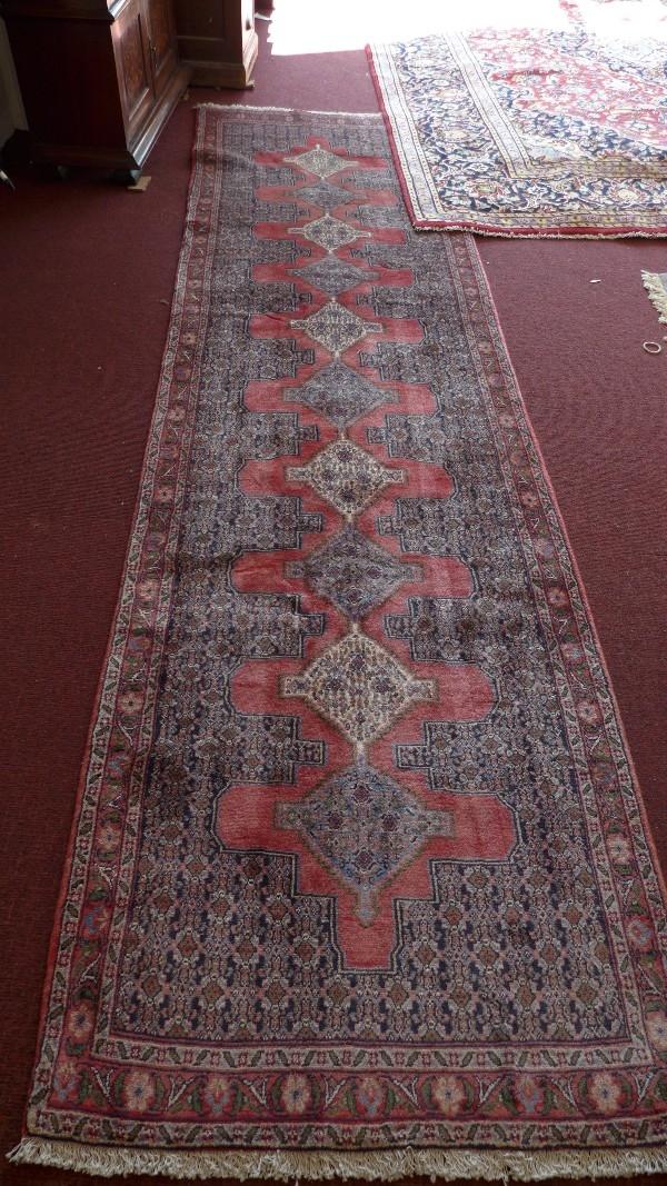 A fine North West Persian Senneh runner, repeating stylised pole medallion all over on a rouge field