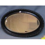 A 20th century oval mirror, having bevelled glass plate within ebonised frame with carved