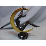A cast bronze study of a nude lady hanging on a polished brass crescent moon, raised on circular