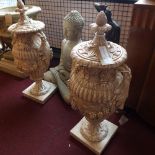 A pair of cast plaster twin handled urns and covers, decorated with grape vines, raised on square