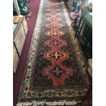 An Afghan runner carpet, having red geometric central medallions on a navy ground, approximately 398