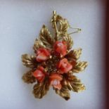 An 18ct yellow gold vintage brooch in the form of a leaf with central coral rose flower heads,