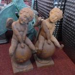A pair of cast iron cherubs seated on globes, raised on socle bases, H.37cm (2)