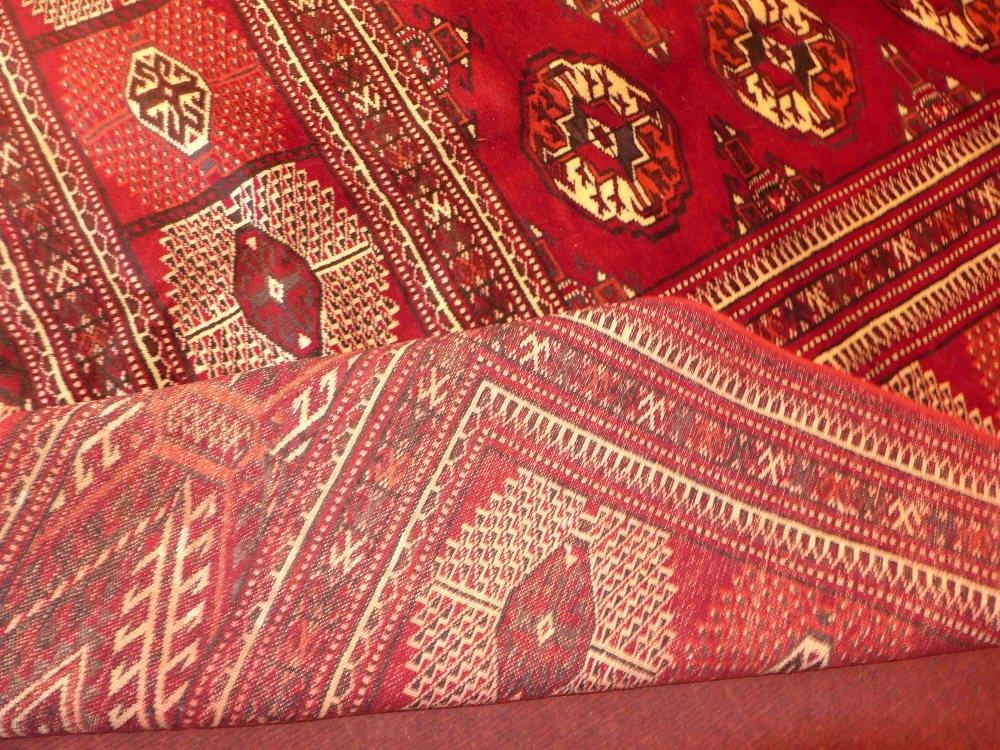 A North East Persian Turkoman carpet, repeating Tekkeh motifs on a madder ground within stylised - Image 2 of 3