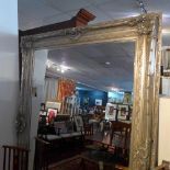 A large mirror with bevelled glass plate, in silver painted frame decorated with flowers and C-