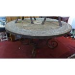 A wrought iron circular garden table, with inlaid stone top, raised on scroll legs