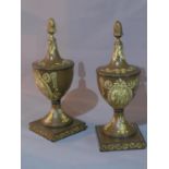 A pair of toleware urns, decorated with scrolling foliage, having brass finials, raised on square