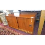 A mid 20th century teak low cabinet, with two sliding doors, raised on castors, H.46 W.82 D.40cm