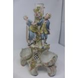 A Sitzendorf style figural candlestick, the stem encrusted with flowers and having three figures,