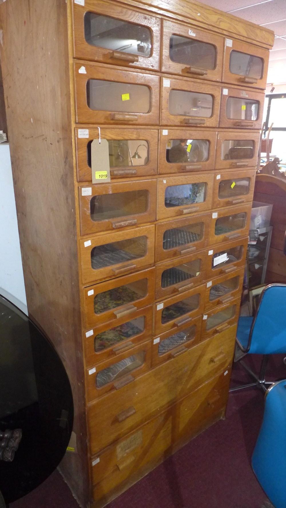 An early to mid 20th century light oak Haberdashery cabinet with 24 glass fronted drawers, above two