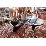 A Noguchi style coffee table with glass top raised on folding ebonised base